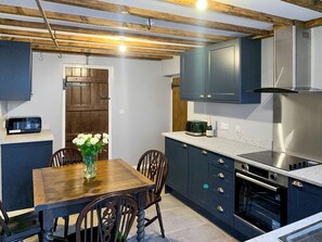 Een moderne keuken met donkere kastjes, een houten eettafel en een vaas witte bloemen.
