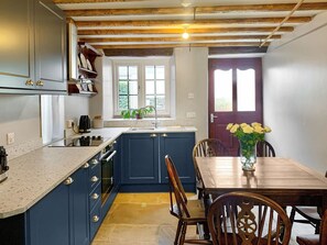 A kitchen with blue cabinets, a wooden dining table, and a vase of yellow flowers.