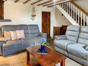 Un salon avec deux canapés gris, une table basse en bois et une décoration en macramé suspendue.