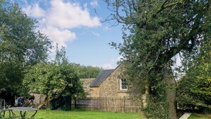 A stone house with a small window and a sloped roof, surrounded by a wooden fence and lush greenery. - 3 bedroom accommodation in Leek (Leek)