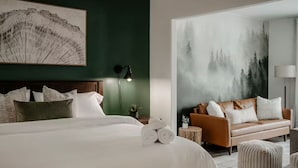 A bedroom with a large bed, a brown leather sofa, and a painting of a forest.