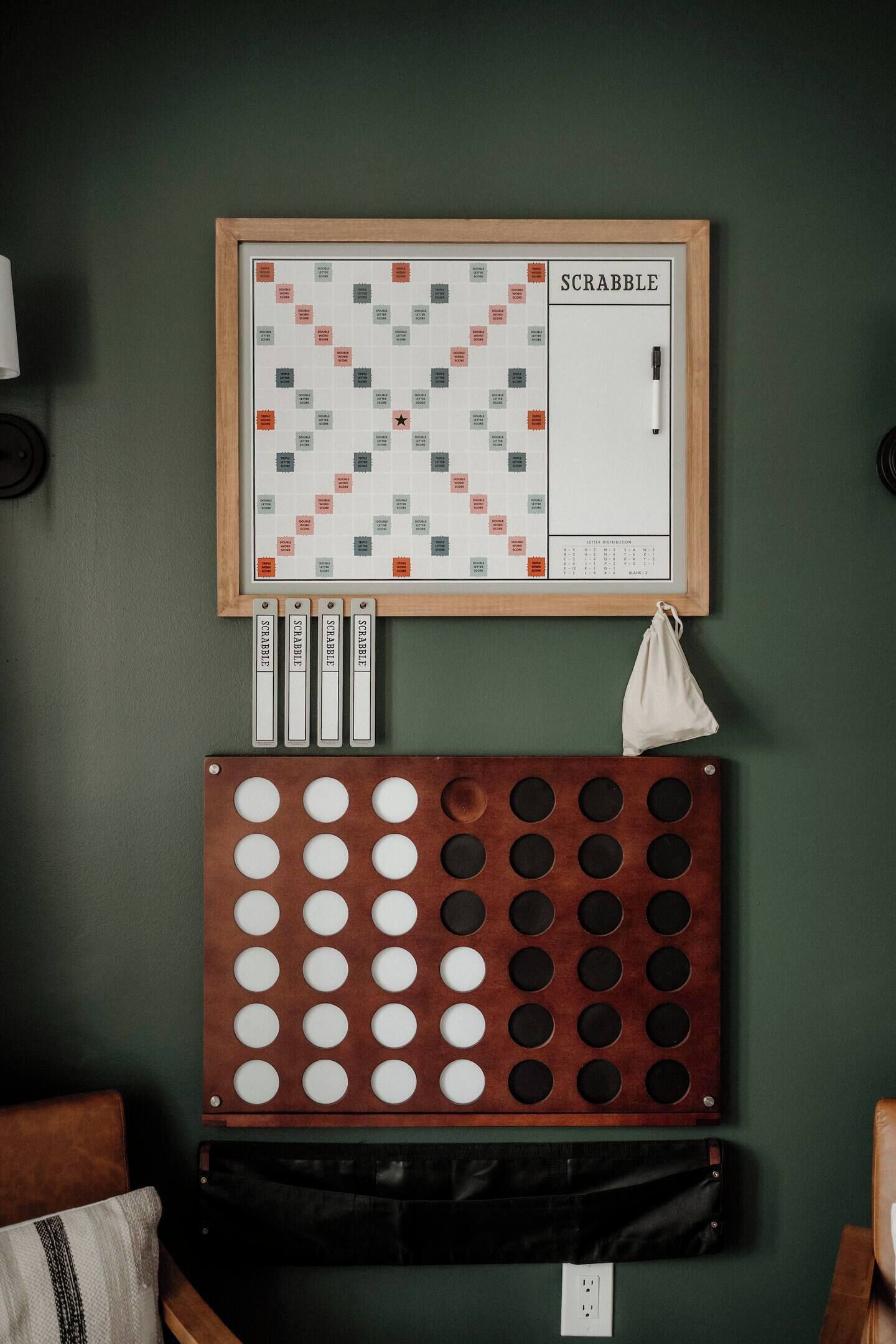 A Scrabble board game set up on a green wall, with tiles and a bag of letters below.