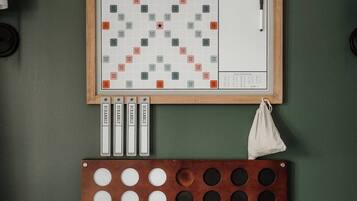 A Scrabble board game set up on a green wall, with tiles and a bag of letters below.