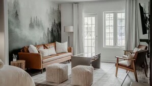 A modern living room with a sofa, ottomans, a coffee table, and a large window with curtains.