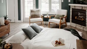 A cozy bedroom with a large bed, two chairs, a fireplace, and a dining table.