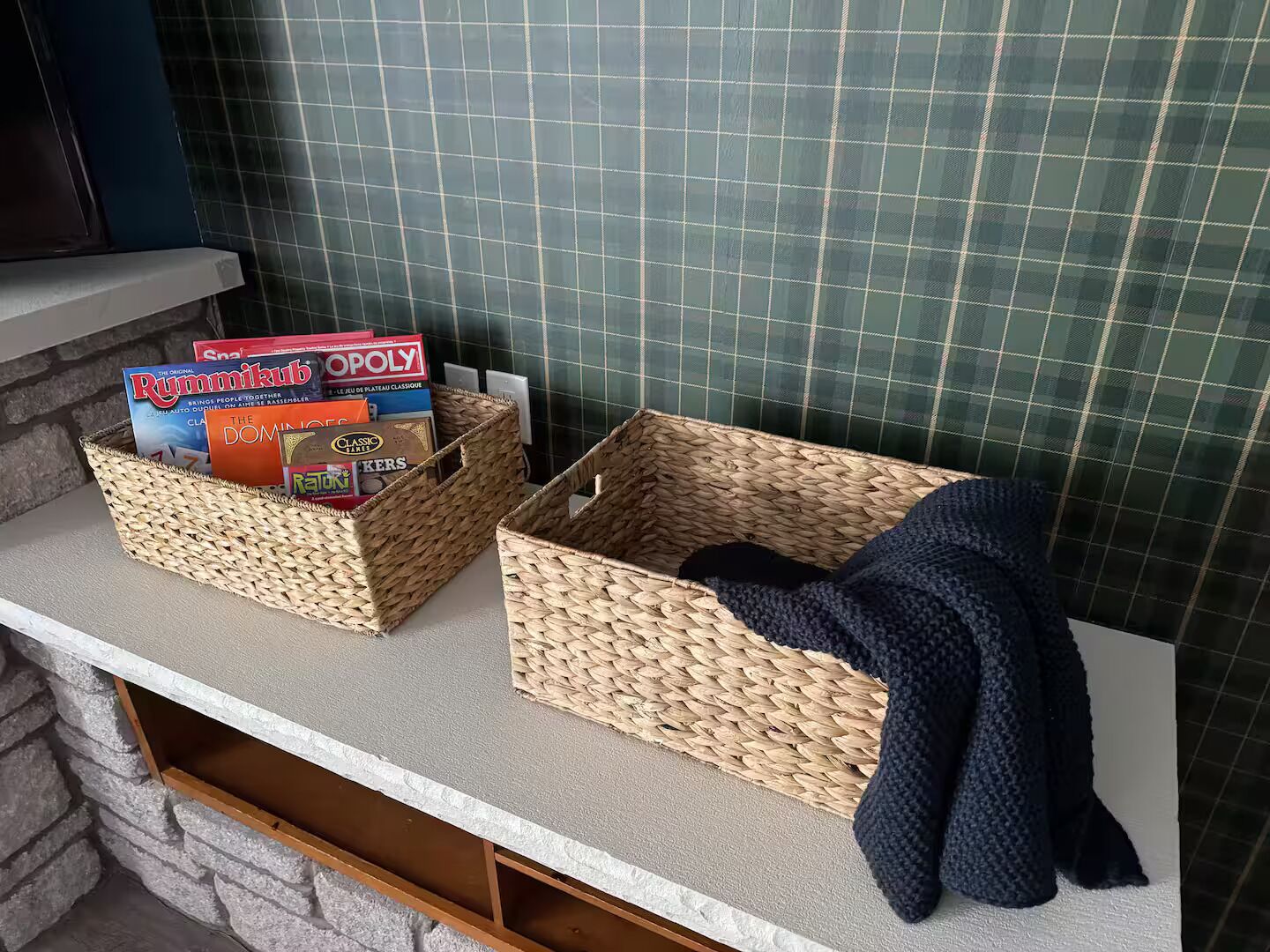 Two woven baskets on a counter with board games and a blanket.