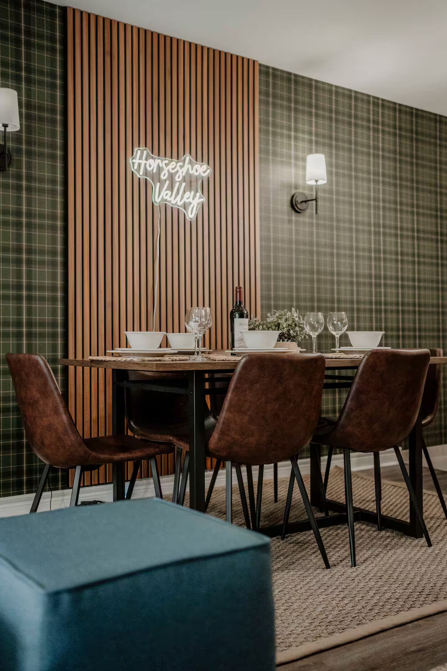 A dining area with a wooden table set for four, accompanied by brown chairs. A neon sign reads "Horseshoe Valley."