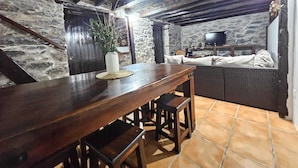 Un coin repas rustique avec une table et des chaises en bois, un mur en pierre et un téléviseur en arrière-plan.