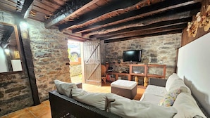 Une pièce rustique avec des murs en pierre, un canapé en osier, un téléviseur et un meuble en bois.