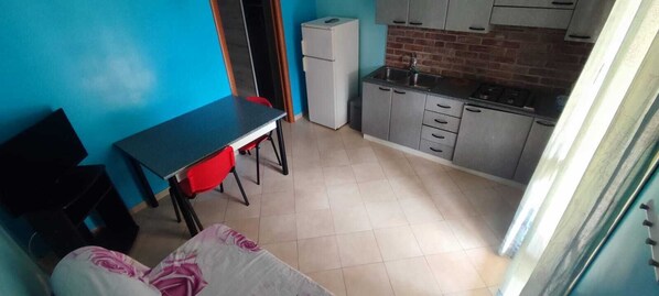 A compact kitchen with a refrigerator, sink, and cabinets. There is a small dining area with a table and chairs. - Villa More - Pool & Nature (Monteroni di Lecce)