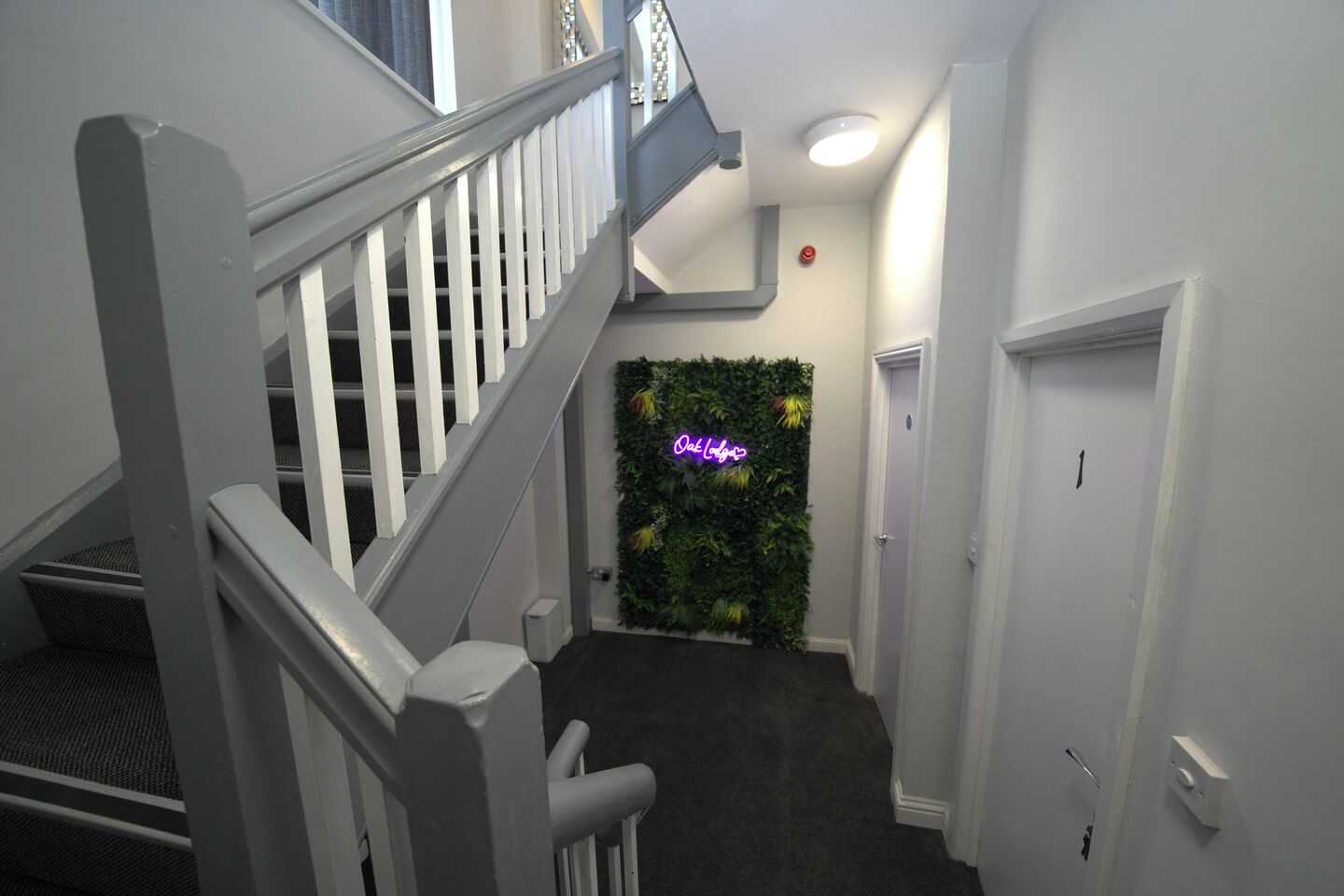 Eine Treppe mit weißen Geländern führt zu einem Raum mit grüner Wand und einem Neonzeichen.