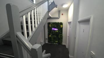 Eine Treppe mit weißen Geländern führt zu einem Raum mit grüner Wand und einem Neonzeichen.