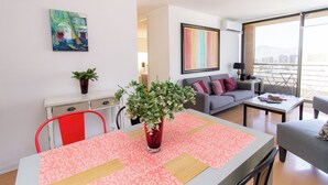 Ein modernes Wohnzimmer mit Essbereich, einem grauen Sofa, einem roten Sessel und einem großen Fenster mit Blick auf die Stadt.