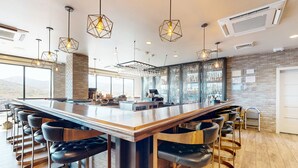 Un espace bar moderne doté d’un long comptoir, de nombreux tabourets et d’un éclairage suspendu.