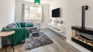A modern living room with a sofa, a small table, a fireplace, and a TV mounted on the wall. - 2 bedroom accommodation in Brixham (Brixham)