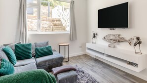 A modern living room with a sofa, a small side table, a flat-screen TV, and decorative fish sculptures. - 2 bedroom accommodation in Brixham (Brixham)