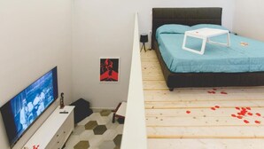 Ein Schlafzimmer mit einem Bett, einem Fernseher, einem kleinen Tisch und einem an der Wand hängenden Bild.