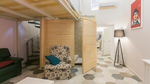 Ein Zimmer mit einer Holzwand, einem gemusterten Sessel, einer grünen Couch, einem weißen Tisch und einem Boden mit sechseckigen Fliesen.