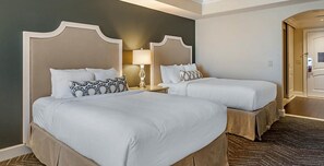 Two comfortable beds with white headboards and matching bedding, a nightstand with a lamp, and a door leading to a larger area.