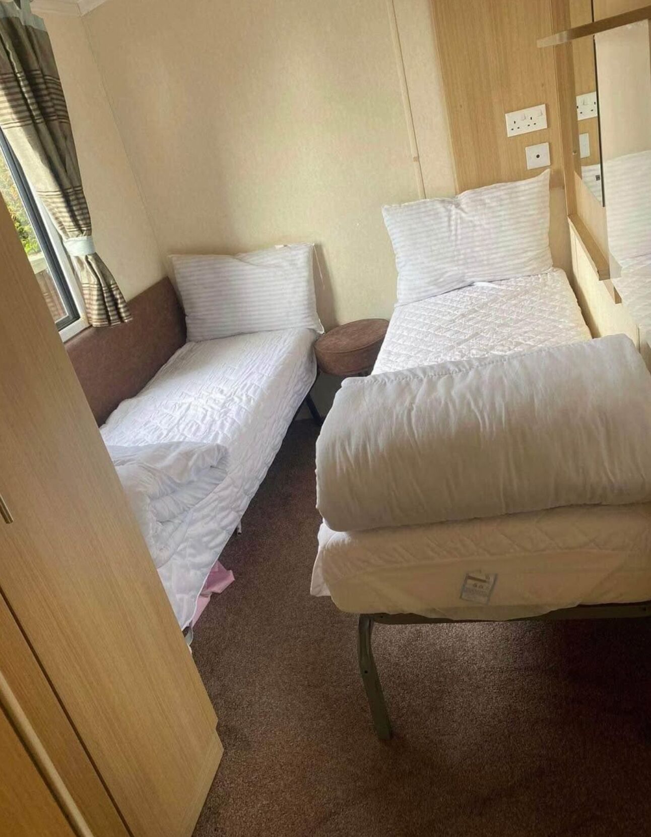 Ein kompaktes Schlafzimmer in einem Wohnmobil mit zwei Betten, einem kleinen runden Tisch und einem Fenster mit Vorhängen.