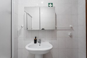 Un baño con lavamanos blanco, un espejo y un armario arriba.