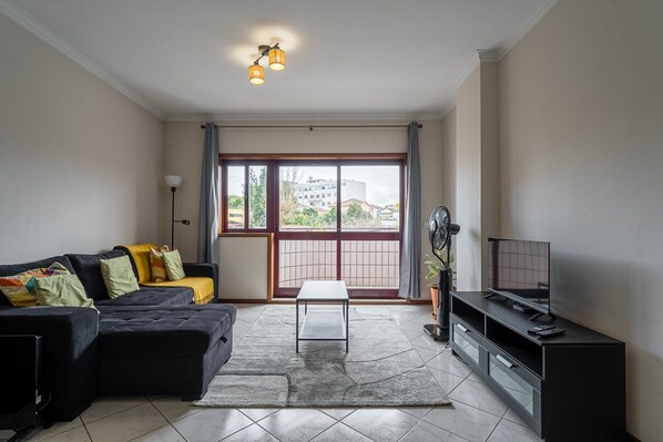 Una sala de estar con un sofá, un televisor, un ventilador y vistas a través de un gran ventanal.