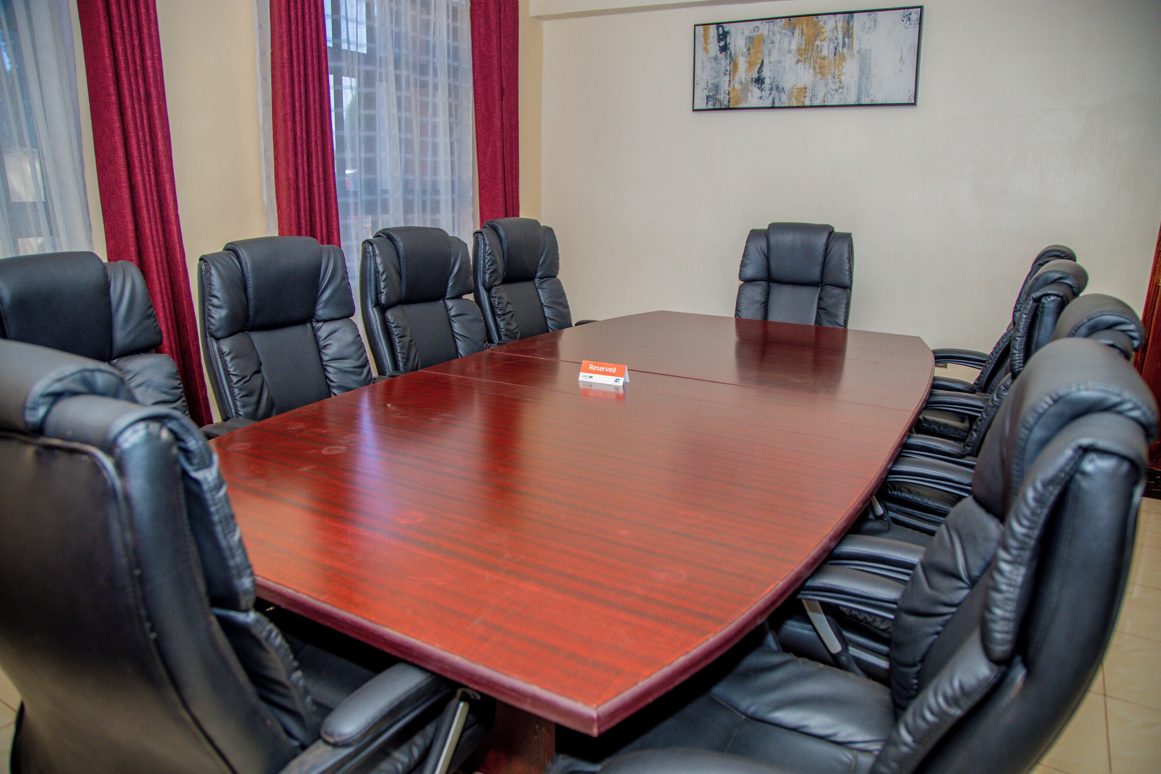 A conference room with a large wooden table and black leather chairs.