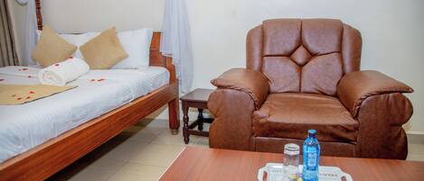 A bedroom with a bed, a wooden nightstand, a brown leather armchair, and a tray with a bottle and glasses.