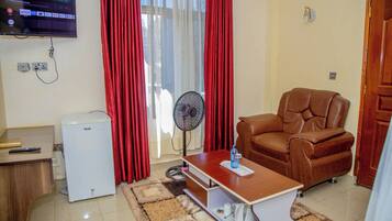 Een woonkamer met een televisie, een ventilator, een leren fauteuil, een kleine koelkast en een salontafel.
