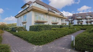 A modern multi-story residential building with a paved pathway and well-maintained hedges. - Apartment Near Belgian Coast With Terrace (Koksijde)