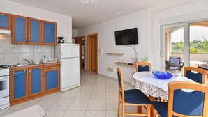 A modern kitchen with blue cabinets, a white refrigerator, and a dining area with a table and chairs. - Bright Apartment in Medolino (Medulin)
