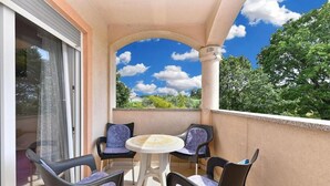 A balcony with a table and four chairs, a sliding glass door, and a view of trees and sky. - Bright Apartment in Medolino (Medulin)