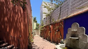 A narrow alleyway with a brick pathway, a white metal bench, and a stone fountain. - La Casa del Árbol - Oaxaca Historic Center (Oaxaca de Juárez)
