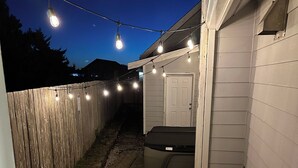 A backyard with a wooden fence, a red Adirondack chair, a barbecue grill, and string lights. - 3BR 1.5Ba - Private Hot Tub & Game Room!! 2 Pets stay free! (Ocean Shores)