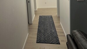 A hallway with a black patterned rug, a ceiling light, and a thermostat on the wall. - 3BR 1.5Ba - Private Hot Tub & Game Room!! 2 Pets stay free! (Ocean Shores)