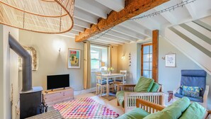 A cozy living room with a fireplace, a dining area, and a large window. - 4 bedroom accommodation in Sedbergh (Sedbergh)
