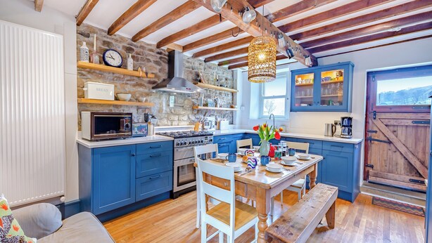 A rustic kitchen with blue cabinets, a wooden bench, and a stone wall. - 4 bedroom accommodation in Sedbergh (Sedbergh)