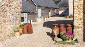 A stone building with a gravel courtyard, rustic wooden walls, and a metal gutter. - The Dairy at Wyke Farm (Axminster)
