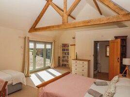 Une chambre avec un plafond en pente, un lit recouvert d’une couverture rose, une commode en bois, une bibliothèque et une porte donnant sur une autre pièce.