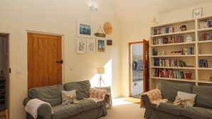 A living room with two grey sofas, a bookshelf, and a door leading to a garden. - The Dairy at Wyke Farm (Axminster)
