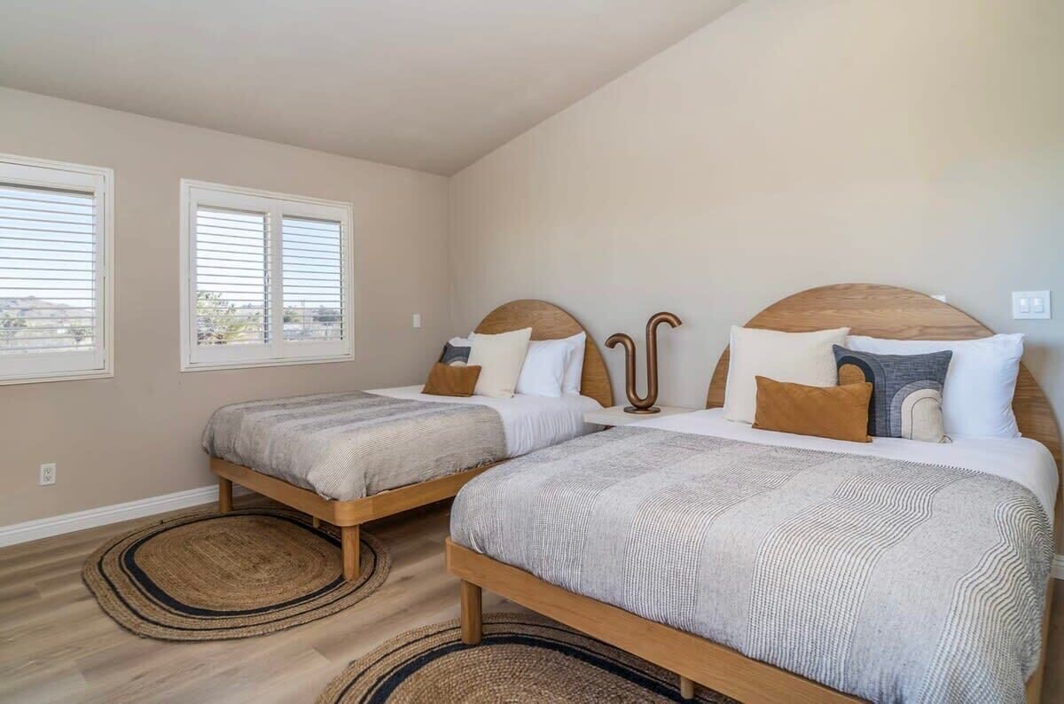 Une chambre avec deux lits, des têtes de lit en bois et une grande fenêtre.