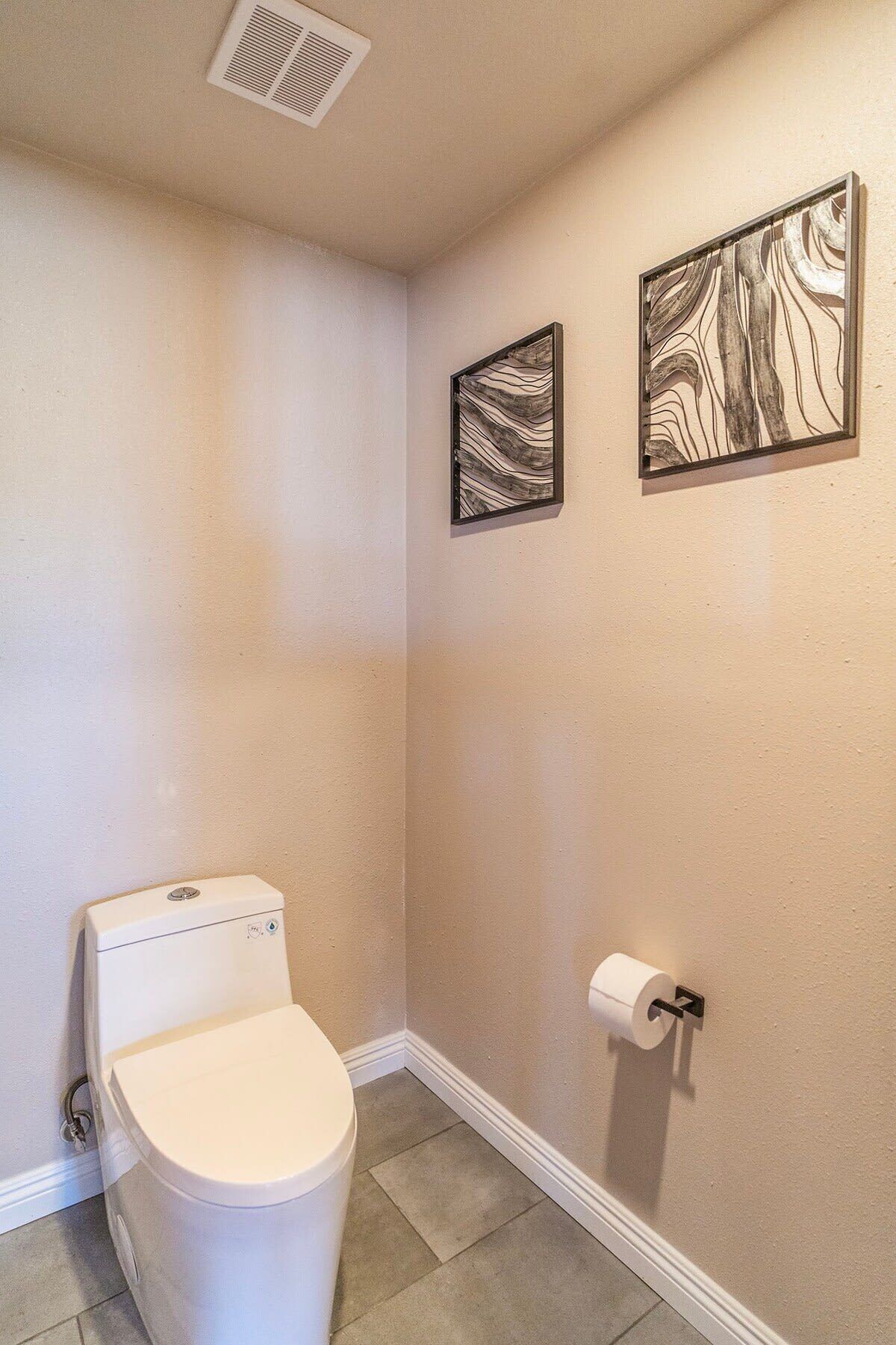 A small bathroom with a toilet, a wall-mounted toilet paper holder, and two framed wall art pieces.