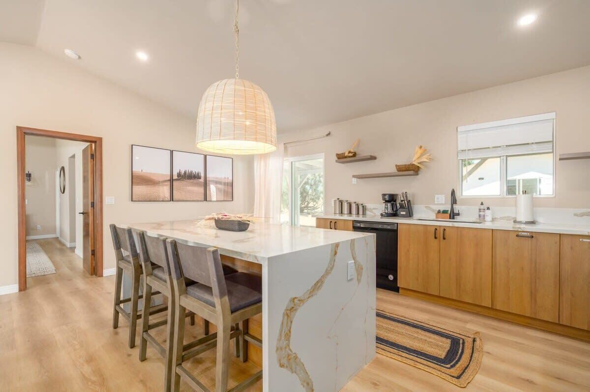 Une cuisine moderne avec un îlot en marbre, des armoires en bois et un luminaire suspendu.