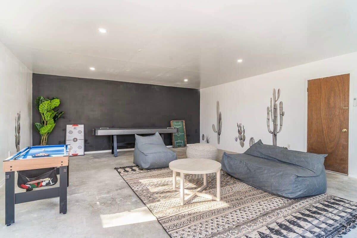 Uma sala de estar moderna com uma mesa de futebol, um sofá, uma mesa de centro e uma TV fixada na parede.