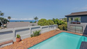 Une piscine avec vue sur l’océan, entourée d’un mur blanc et d’une terrasse en briques.