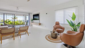 Un salon moderne doté d’une grande fenêtre, d’un ventilateur de plafond et d’un téléviseur à écran plat fixé au mur.