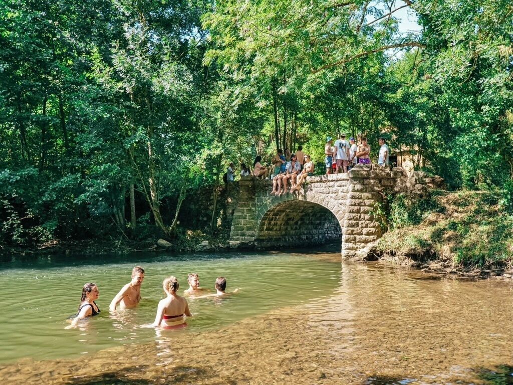 Eine Steinbrücke über einem Fluss, auf dem Menschen schwimmen und stehen.