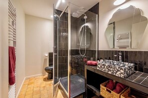 Un baño moderno con ducha de vidrio, tocador con lavamanos de mosaico y un espejo grande.