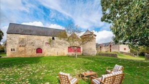 A stone building with a red door and windows, surrounded by a grassy lawn with outdoor furniture.