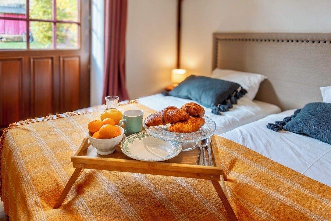 A breakfast tray with croissants, oranges, and a mug on a bed with a plaid blanket.